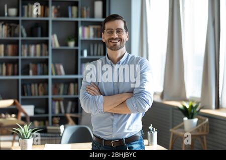 Portrait laughing businessman with arms crossed standing in modern cabinet Stock Photo