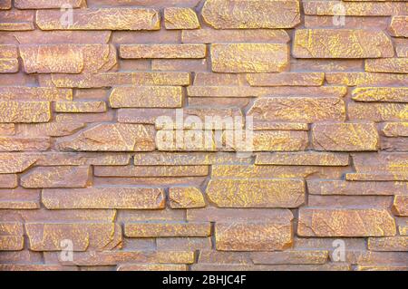 Modern stone brick wall is painted with brown and gold paint, for use as background and texture. Stock Photo