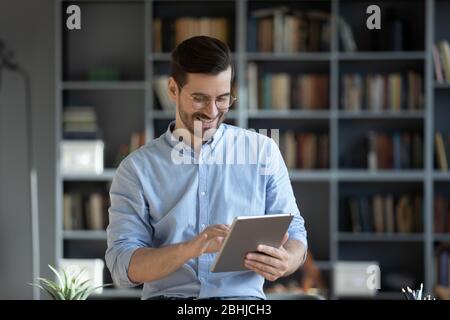 Smiling businessman wearing glasses using computer tablet in modern cabinet Stock Photo