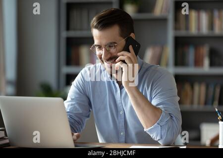 Smiling businessman talking on phone, looking at laptop screen Stock Photo
