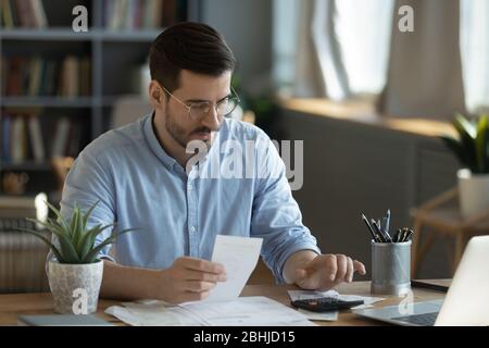 Serious man wearing glasses checking bills, using calculator Stock Photo