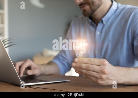 Close up businessman holding light bulb, sitting at work desk Stock Photo