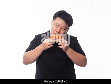 Happy young asian fat man in black polo shirt eating pizza isolated over white background. Stock Photo