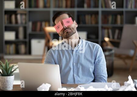 Exhausted tired businessman with stickers on eyes sleeping at workplace Stock Photo