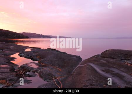 Winter sunset with atmospheric colours and reflections at the rocky shores of Trondheimsfjorden, Flatholmen, Norway. Stock Photo