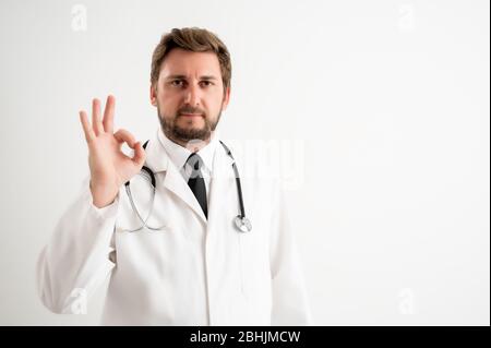 Portrait of male doctor with stethoscope in medical uniform showing OK sign posing on a white isolated background Stock Photo