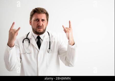Portrait of male doctor with stethoscope in medical uniform doing rock symbol with hands up posing on a white isolated background