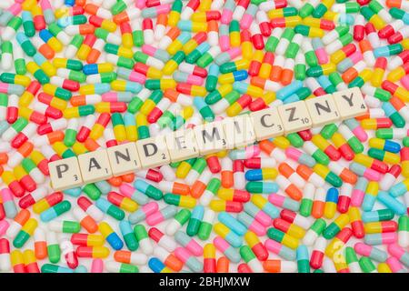 Multicoloured pills caplets & letter tiles: PANDEMICZNY - Polish adjectival form of word Pandemic. Coronavirus conceptual, CV19 / Covid 19 metaphor Stock Photo