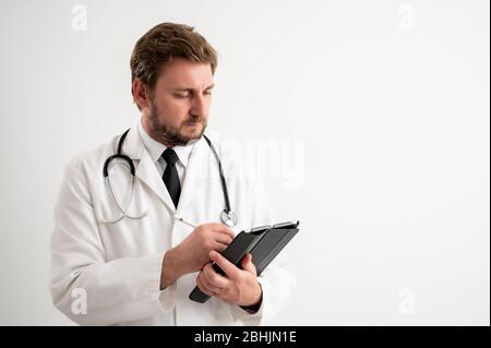 Portrait of male doctor with stethoscope in medical uniform takes notes, posing on a white isolated background Stock Photo