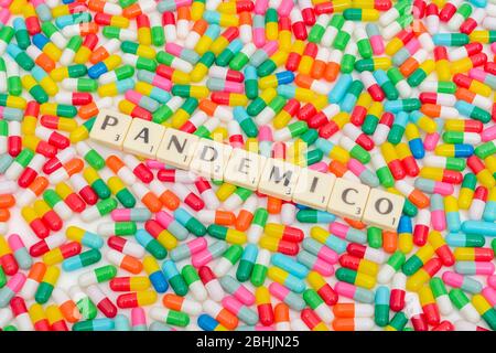 Multicoloured pills caplets and letter tiles: PANDEMICO - Spanish & Italian adjective for Pandemic. Coronavirus conceptual, CV19 / Covid 19 metaphor. Stock Photo