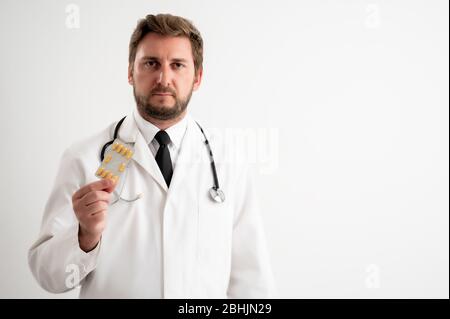 Portrait of male doctor with stethoscope in medical uniform showing yellow drugs posing on a white isolated background. Stock Photo