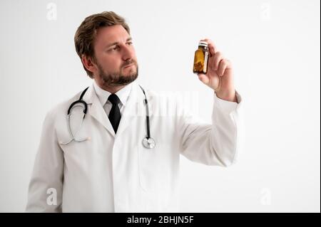 Portrait of male doctor with stethoscope in medical uniform holding dose of pills posing on a white isolated background Stock Photo