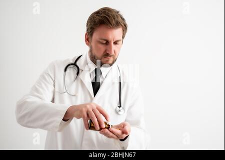 Portrait of male doctor with stethoscope in medical uniform spilling pills from bottle posing on a white isolated background Stock Photo