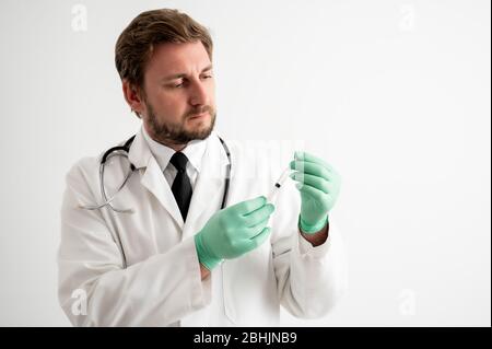 Portrait of male doctor with stethoscope in medical uniform with medical glove and syringe in hand posing on a white isolated background Stock Photo