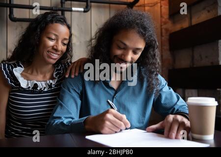 Excited multiethnic couple closing deal with broker in cafe Stock Photo