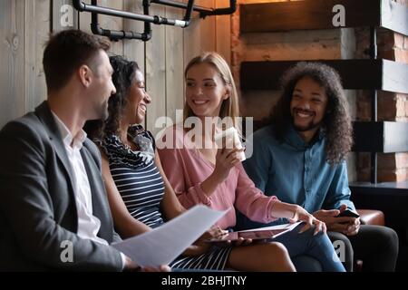 Happy diverse young people sit on couch talking Stock Photo