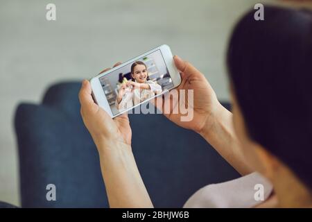 Online video chat with family. Happy daughter girl making hands with heart greets mother using laptop mobile sitting at home. Stock Photo