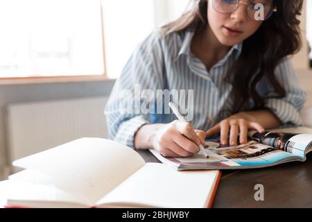 Cropped image of an attractive pensive young brunette woman studying in the cafe indoors, taking notes Stock Photo