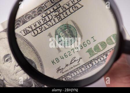 Fake money concept. Cropped close up photo of human finding false cash looking through magnifying glass Stock Photo
