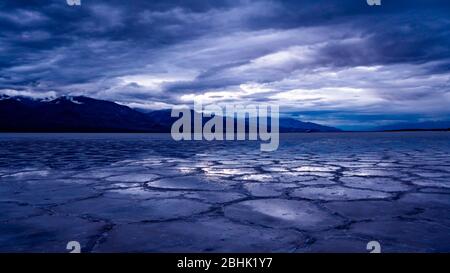 Dramatic sunset skies and reflections in pools that remain after a rare day of rain at Badwater Basin in Death Valley National Park. Stock Photo