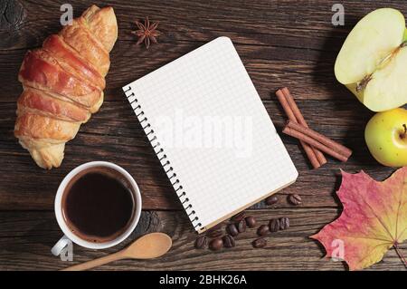 Croissant with coffee, opened notepad and apple on dark wooden table, top view Stock Photo