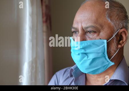 senior man with face mask looking through window  Stock Photo