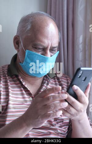 senior man with face mask using smart phone at home  Stock Photo