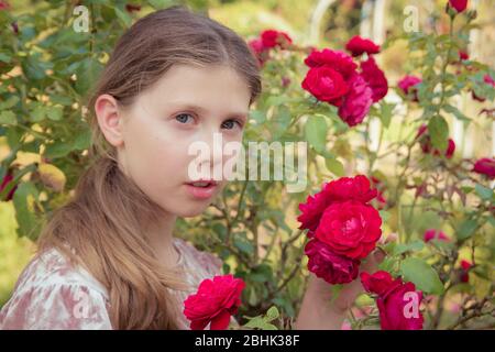 A fresh-faced portrait of a pretty girl holding roses in a summer garden