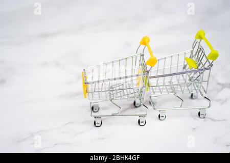 Shopping carts from supermarket on a light white background. Two empty stainless steel small miniature toy shopping trolley on marble table. Shopping Stock Photo