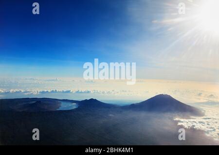 View from airplane window. Aerial photo of Agung - highest peak of island Bali, mount Abang, active volcano Batur with volcanic lake in caldera. Stock Photo