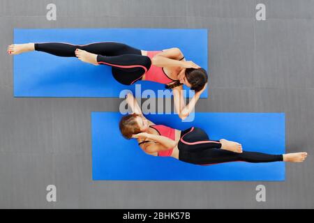 Top view of two young active women with slim body doing bicycle abdominal crunches exercise on yoga mat at group fitness class. Sporty people training Stock Photo