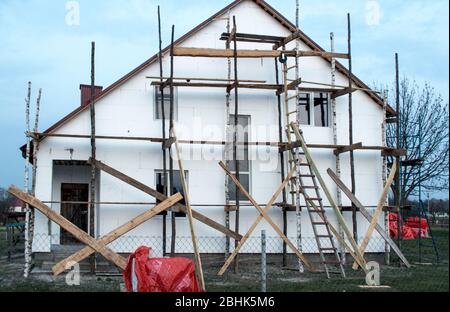 The photo shows a white unfinished white two-storeyed private house on a sky background, scaffolding Stock Photo