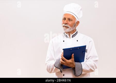 Portrait of senior  chef holding cookbook on gray background. Stock Photo