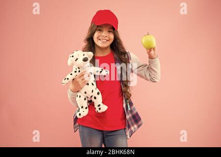 Apple is the happiest vitamin. Happy little girl hold apple and toy on pink background. Small child with healthy apple snack. Eating apple fruit full of vitamin is healthy for learn and play. Stock Photo