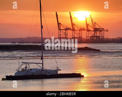 Queenborough, Kent, UK. 26th Apr, 2020. UK Weather: the sun sets behind the cranes of Thamesport as seen from Queenborough, Kent this evening. Credit: James Bell/Alamy Live News Stock Photo