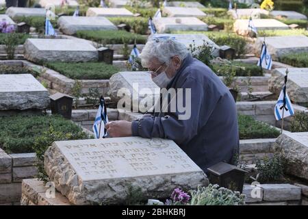 Jerusalem, Israel. 26th Apr, 2020. An Israeli man wearing protective mask due to the COVID-19 coronavirus pandemic grieves over the grave of a loved one at the national military in Mount Herzl in Jerusalem as Israel prepares to mark the memorial day for fallen soldiers. Official ceremonies will not take place this year due to a national curfew to combat the COVID-19 pandemic. Stock Photo