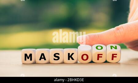 Hand turns dice and changes the expression 'mask off' to 'mask on'. Stock Photo