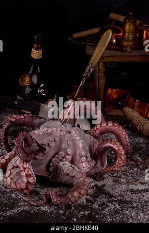 Big octopus against of on dark background with old vintage dishes and bottle of rum. Preparation delicious dinner. Stock Photo