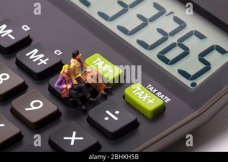 Conceptual image of miniature figure people sat on a calculator next to buttons marked tax