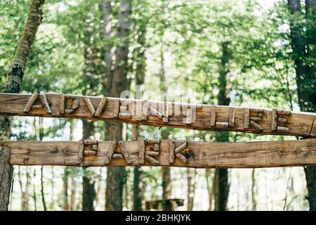 lettering Adventure park. Wooden inscription on a tree - ADVENTURE PARK, against the background of a blurous forest Stock Photo
