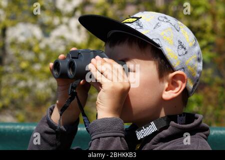 Lockdown activity - boy child kid looking through binoculars standing on balcony Stock Photo