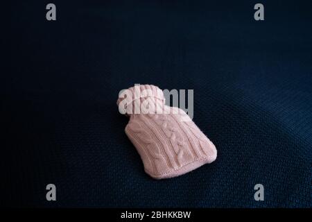 Medical hot-water bottle. Medical heating pad in a wool case of pink wool rests on a plaid of blue Stock Photo
