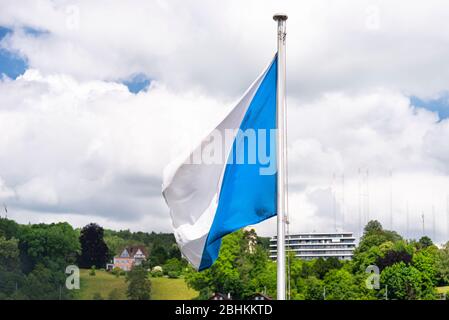 A white and blue flag hanging on the mast slightly fluttering to the left, white clouds in the background. Stock Photo