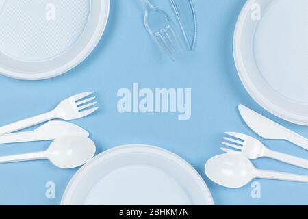 Disposable plastic dishes, plates, knives, forks on a blue background. Frame of objects. Environmental pollution, rejection of non-recyclable plastic, Stock Photo