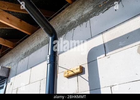 A black metal gutter attached to the raw wall of the house to make a distance to insulate the building. Stock Photo