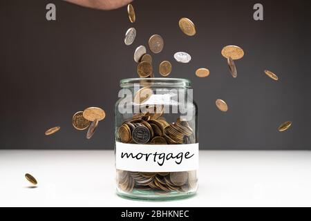 Coins in a jar with mortgage text on a white label. Money falling from the sky above. Savings abstract concept. Copy space. Stock Photo