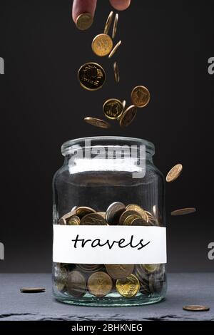 Coins in a jar with travels text on a white label. Caucasian man throwing money from above. Savings abstract concept. Copy space. Vertical orientation Stock Photo