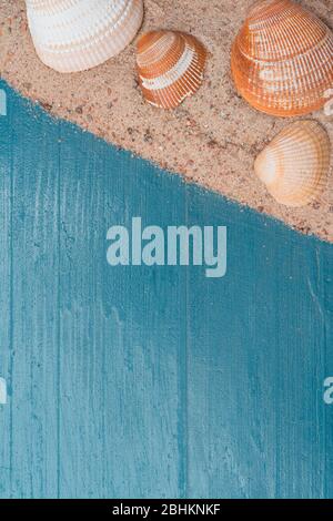 Golden beach sand with seashells on a blue wooden background. Summer travel abstract concept. Copy space on the bottom. Vertical orientation. Stock Photo