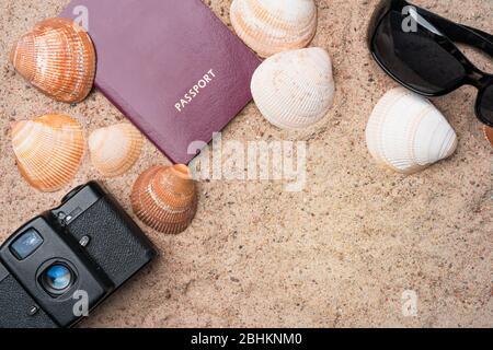 Passport, vintage film camera, sunglasses and seashells on golden beach sand. Summer travel abstract concept. Copy space in the bottom right corner. Stock Photo