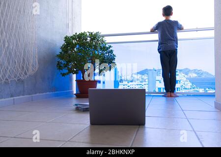 Online learning, distance education, homeschooling, school from home during quarantine. Kid with laptop computer and books on balcony look away Stock Photo